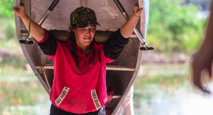 a young person portages a canoe on their shoulders on an outward bound course